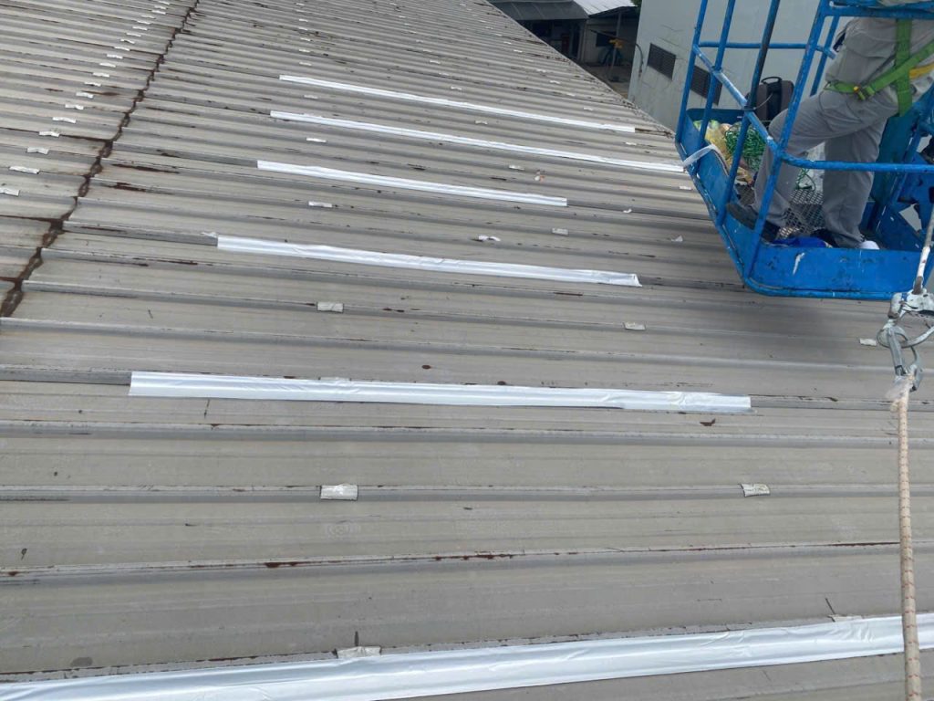 Boom lift used to apply waterproofing tape along a factory roof edge