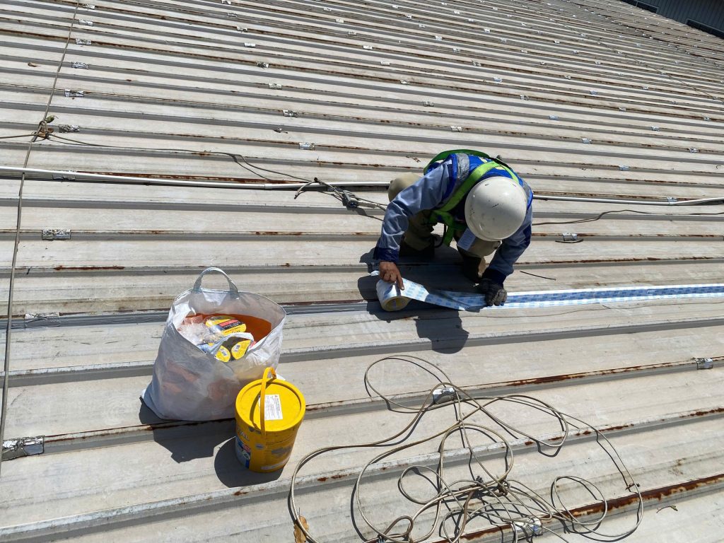 Applying waterproofing tape along metal roof lap joints