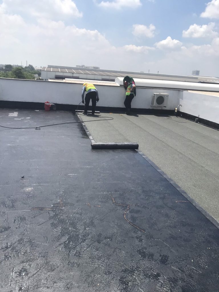 Workers torch-applying mineral-surfaced bitumen membrane on the Compass II office roof