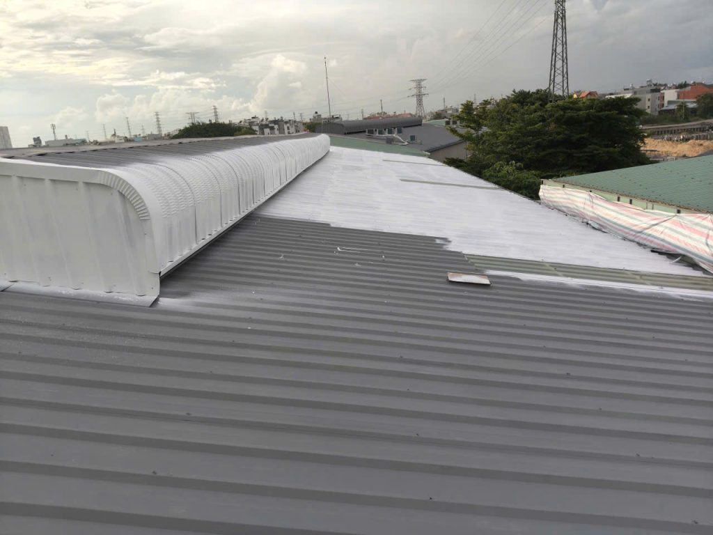 Applying white heat-reflective coating over grey anti-rust primer on a metal roof
